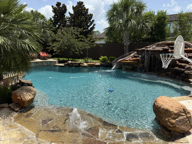 Lagoon-style pool with a rock waterfall grotto and an in-water basketball hoop, kept crystal clear by Lanterra Pools