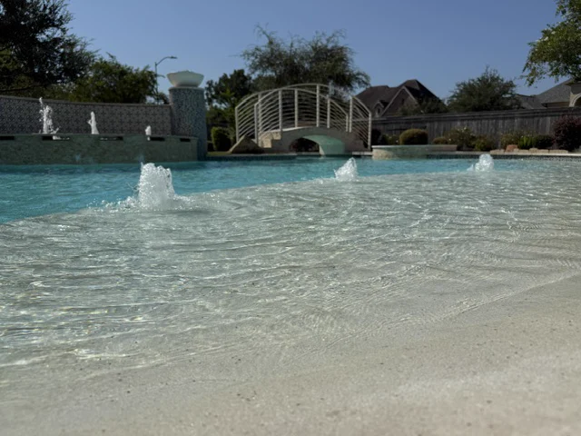 Crystal-clear pool water with deck-jet fountains arcing over a beach entry