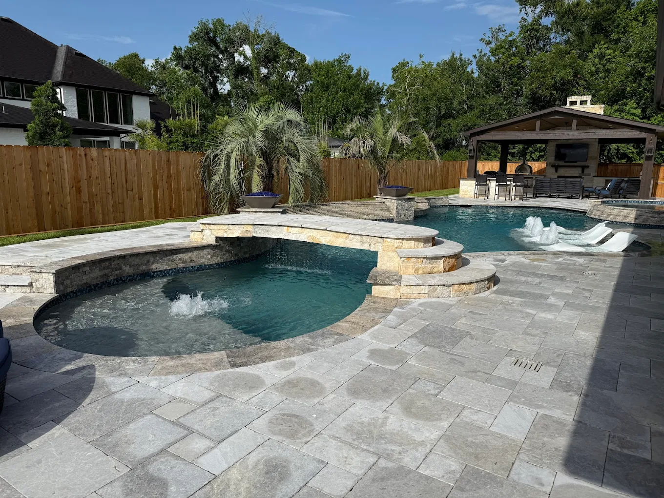 Resort-style backyard pool and spa with travertine decking, built and serviced by Lanterra Pools in the Houston area