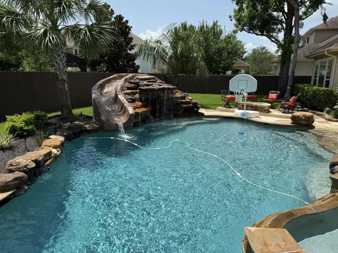 Backyard pool with a rock slide and waterfall, a floating pool cleaner hose, and a fire pit patio